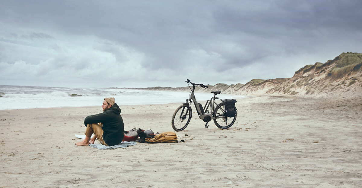 Lease a bike: Mann sitzt am Strand mit abgestelltem Fahrrad neben sich.