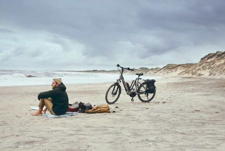Lease a bike: Mann sitzt am Strand mit abgestelltem Fahrrad neben sich.