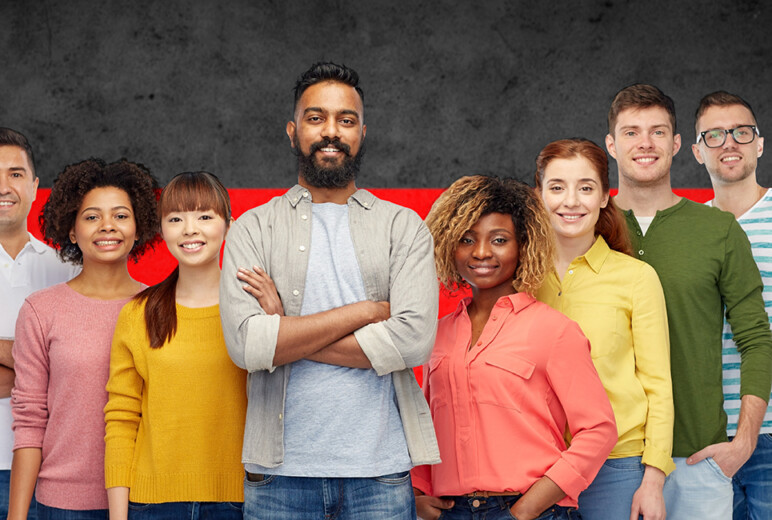 Gruppe junger Menschen unterschiedlicher Herkunft lächelt vor einer Deutschlandflagge.